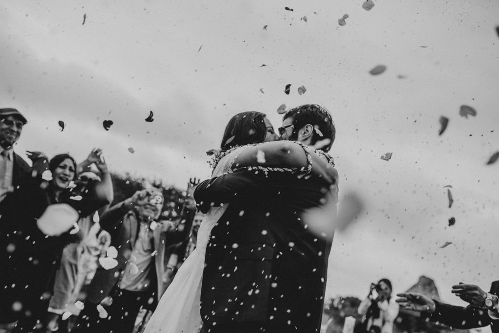 Bride and groom embrace in a shower of flower petals during their outdoor wedding ceremony.